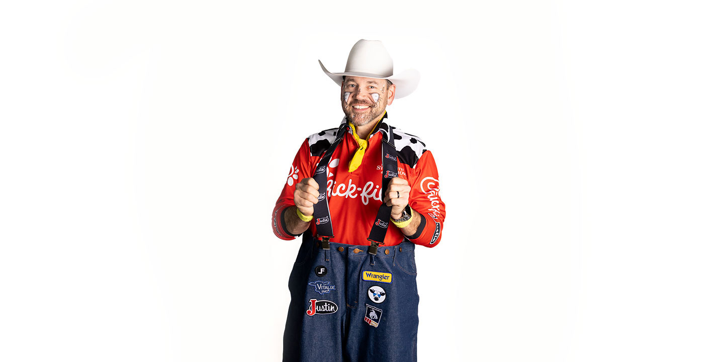 El barrendero profesional Matt Merritt, vestido con una camisa roja, un sombrero de vaquero blanco y sonriendo, sosteniendo las correas de sus tirantes.